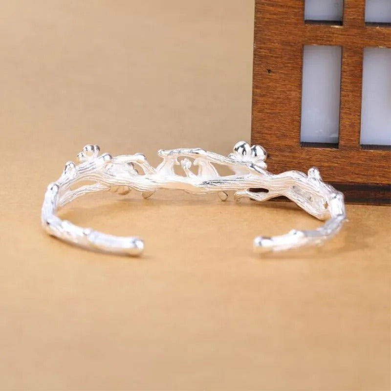 Silver branch-like bracelet on a beige surface with a wooden frame in the background