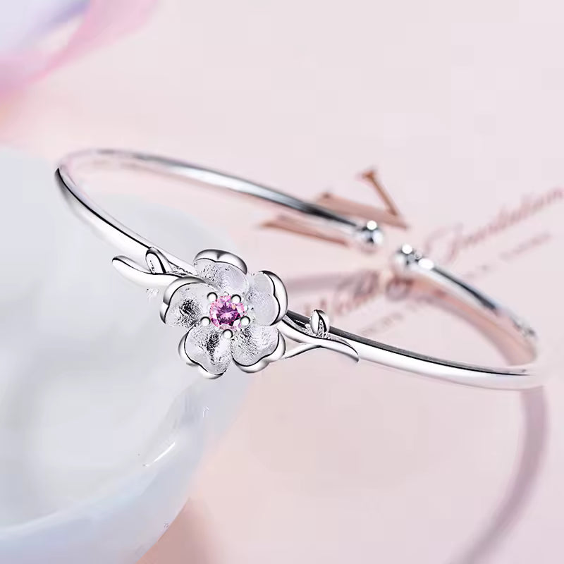 Silver bracelet with a floral design and pink gemstone on a soft pink background