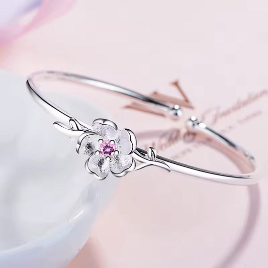 Silver bracelet with a floral design and pink gemstone on a soft pink background