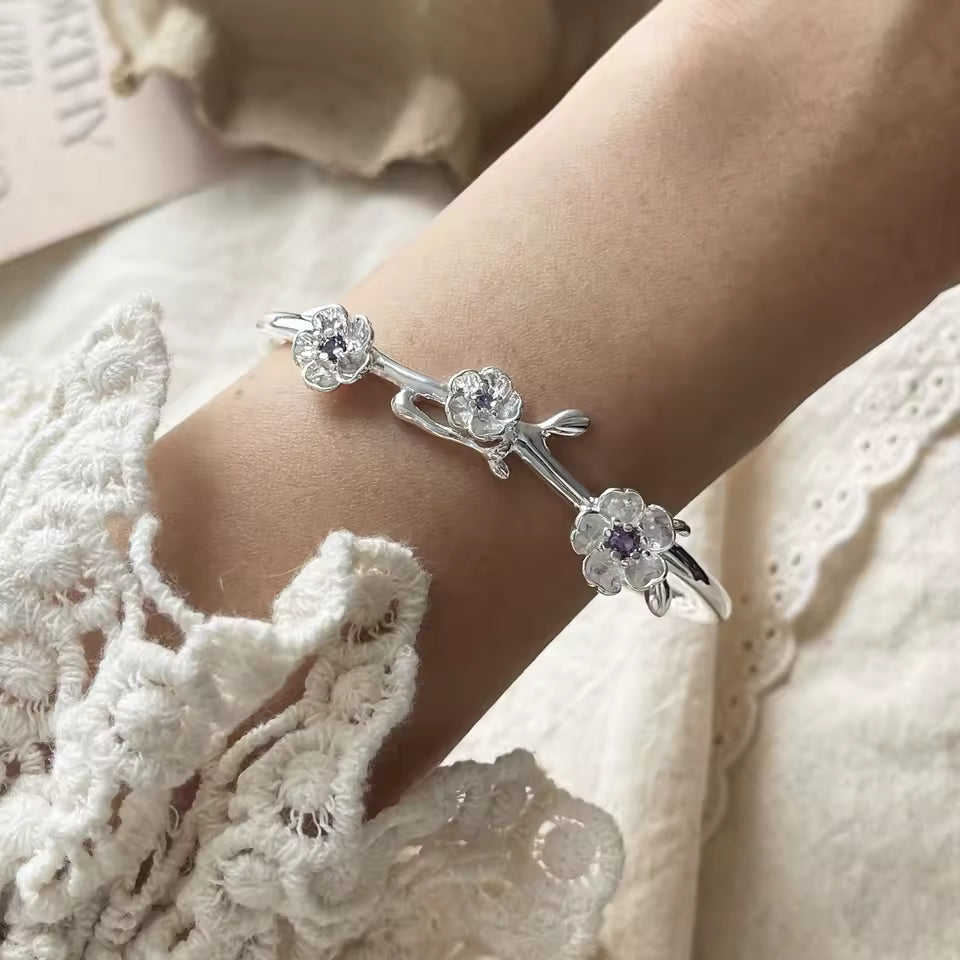 Silver bracelet with floral designs on a person's wrist against a lace garment background