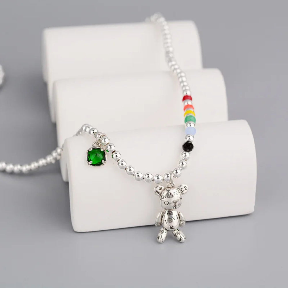Necklace with a teddy bear pendant and colorful beads on a white stand.