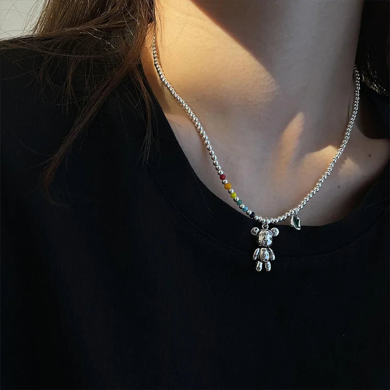 Necklace with a teddy bear pendant worn by a person against a dark background