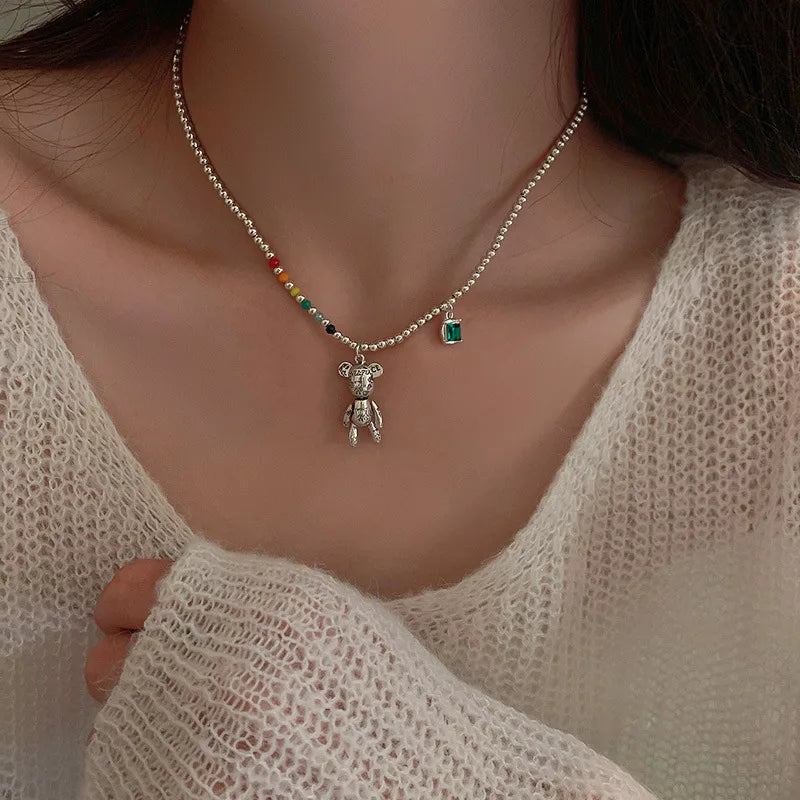 Necklace with a bear pendant and colorful beads worn by a person in a light-colored top.