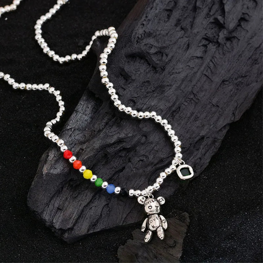 Necklace with colorful beads and a teddy bear charm on dark wood background