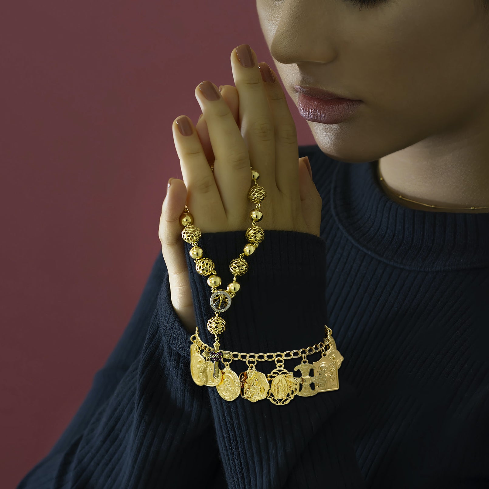Woman wearing a gold necklace with various pendants against a dark background