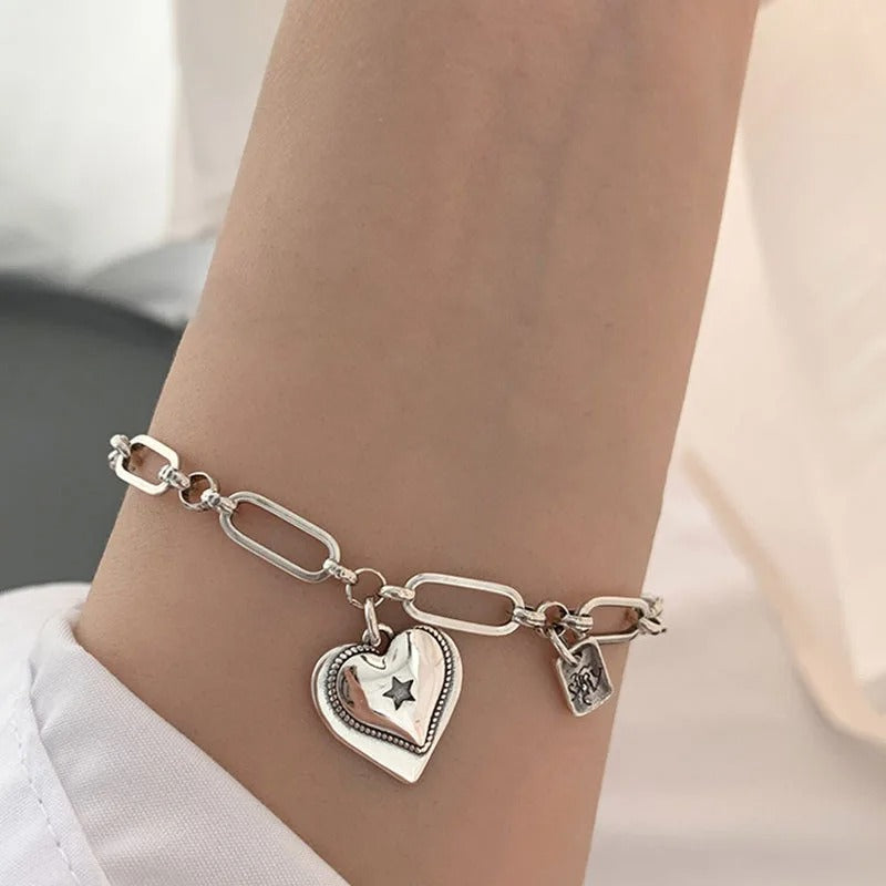 Silver bracelet with heart-shaped charm on a wrist against a neutral background