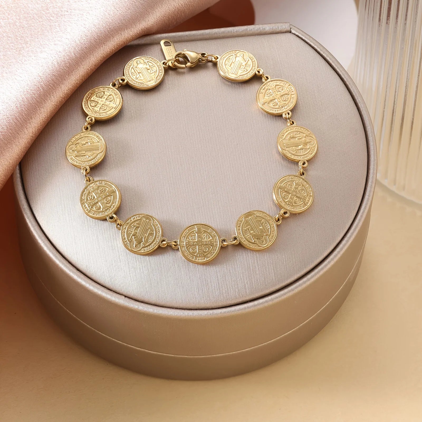 Gold bracelet with coin-like charms on a beige cushioned box
