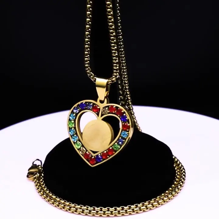 Gold necklace with a heart-shaped pendant featuring colorful stones on a black stand.