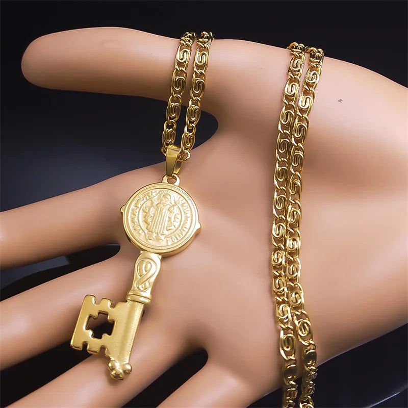 Gold key-shaped pendant and chain on a mannequin hand against a dark background