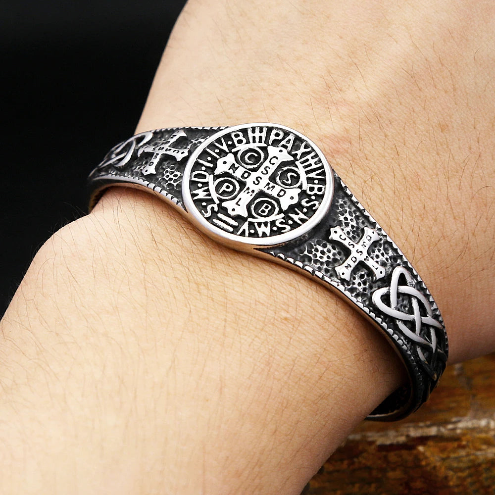Silver bracelet with intricate designs on a wrist against a dark background