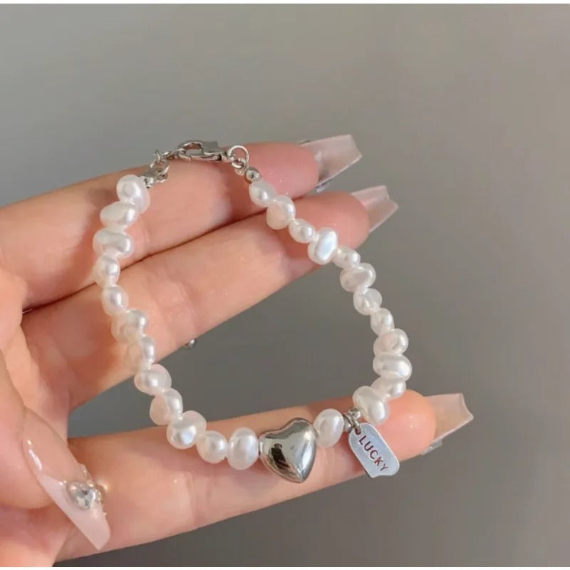 Pearl bracelet with a heart-shaped charm and 'Lucky' tag held by a hand against a neutral background