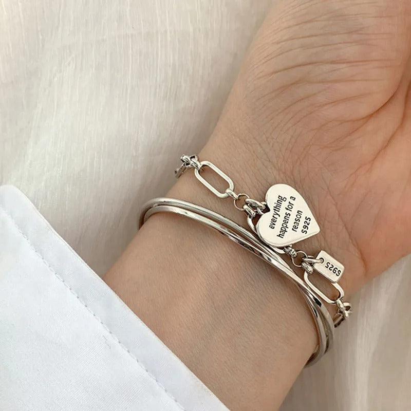 Silver bracelet with heart-shaped charm on a wrist against a white background