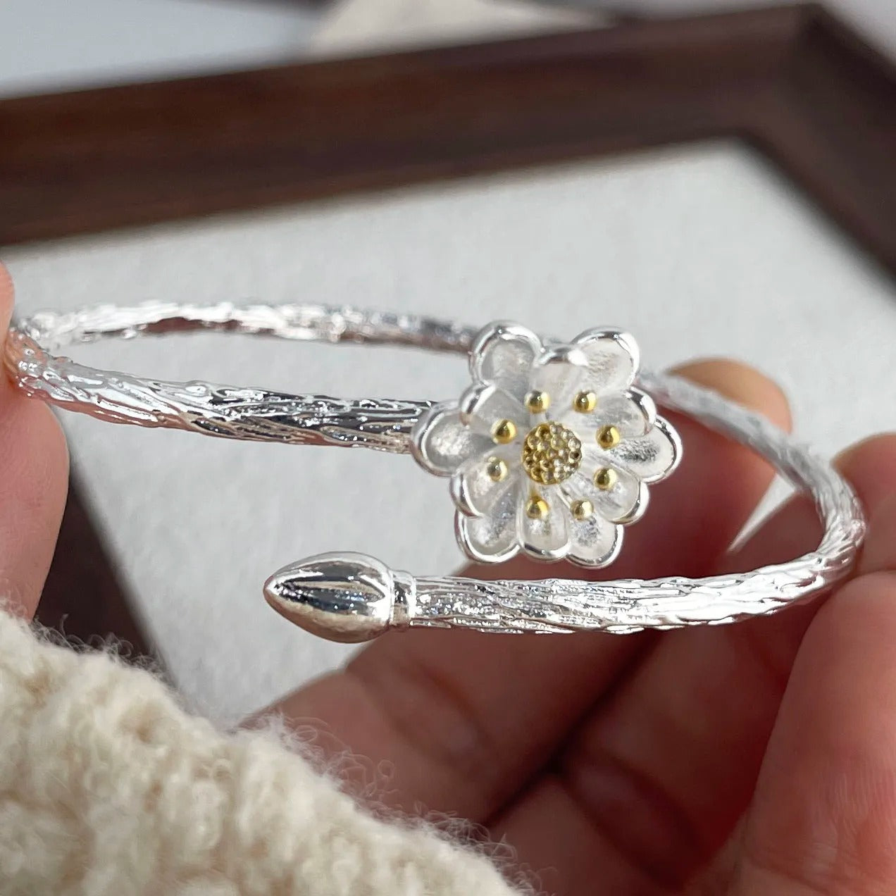 Silver bracelet with a floral design held by a hand