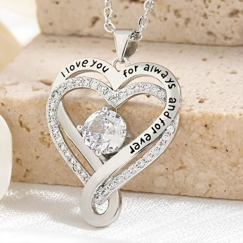 Silver heart-shaped pendant with engraved text on a beige stone background