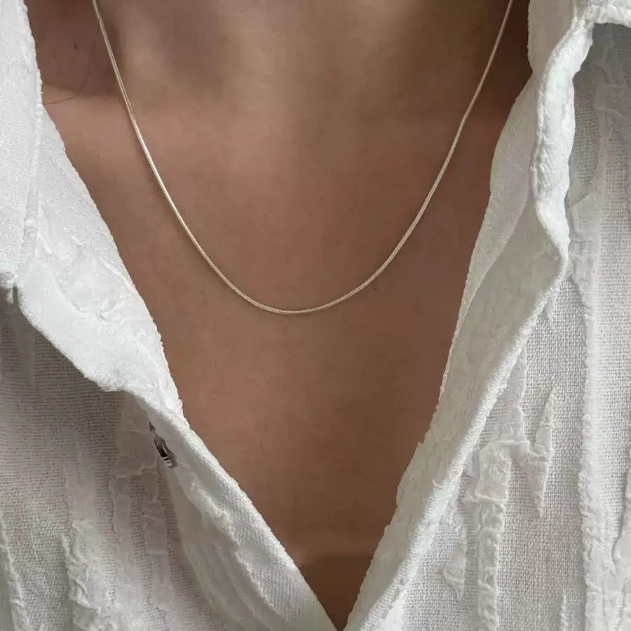 A silver necklace worn by a person with a white garment