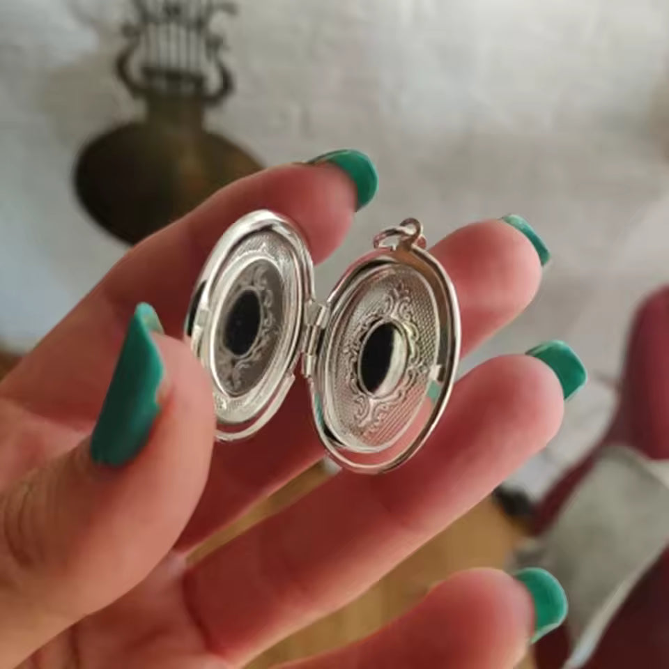 Silver locket held between fingers with a blurred background