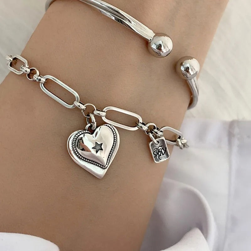 Silver bracelet with heart-shaped charm on a wrist against a white background