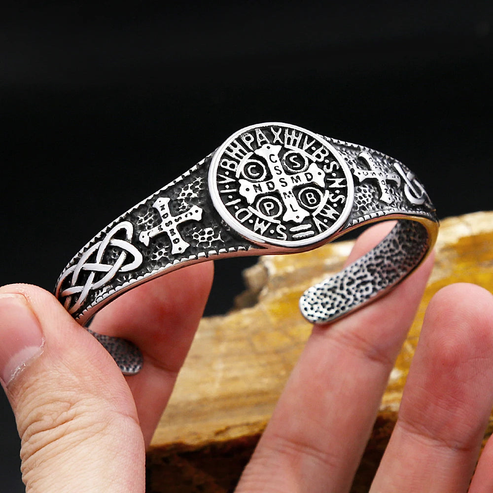 Silver bracelet with intricate designs held by a hand against a dark background