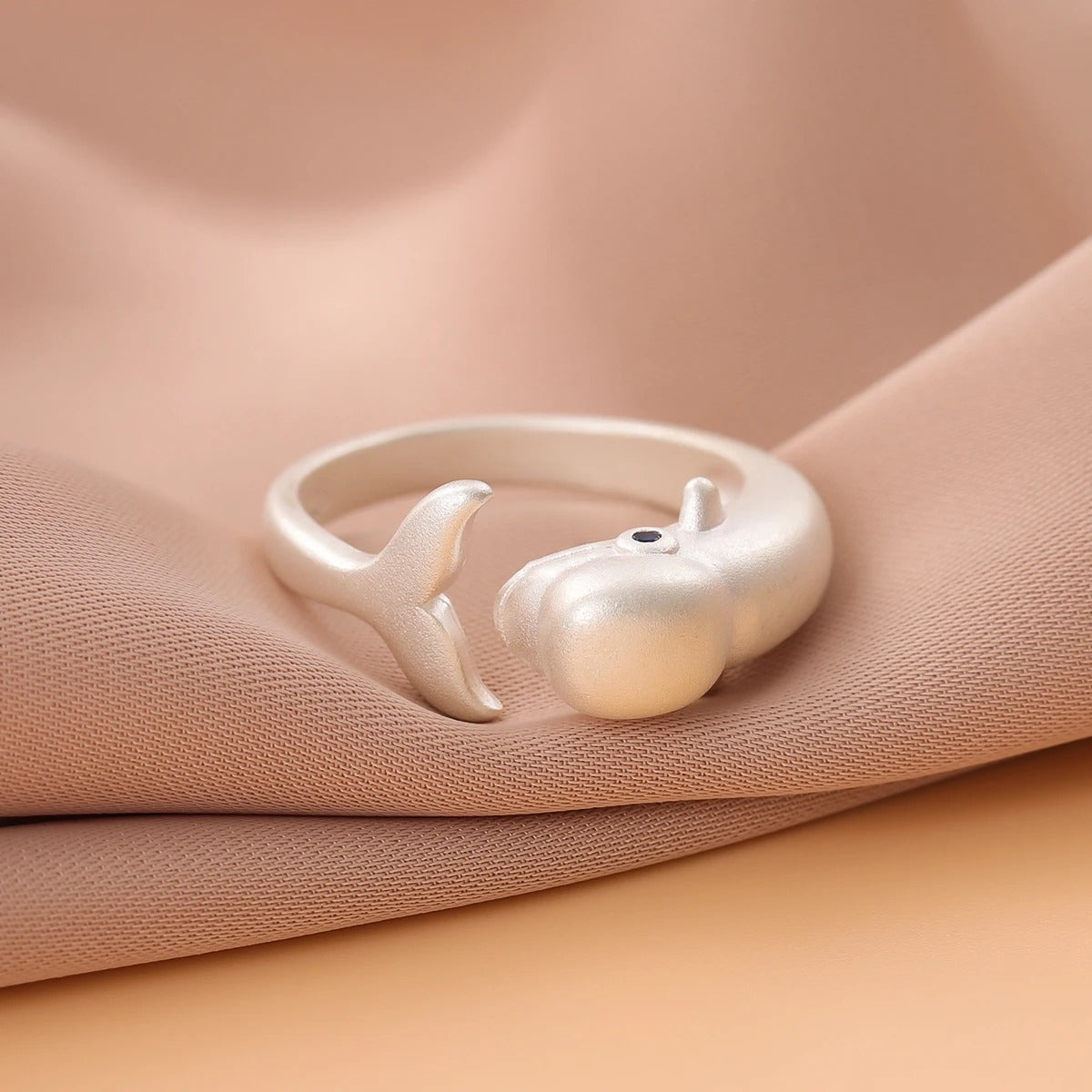 Silver ring with dolphin design on a beige fabric background