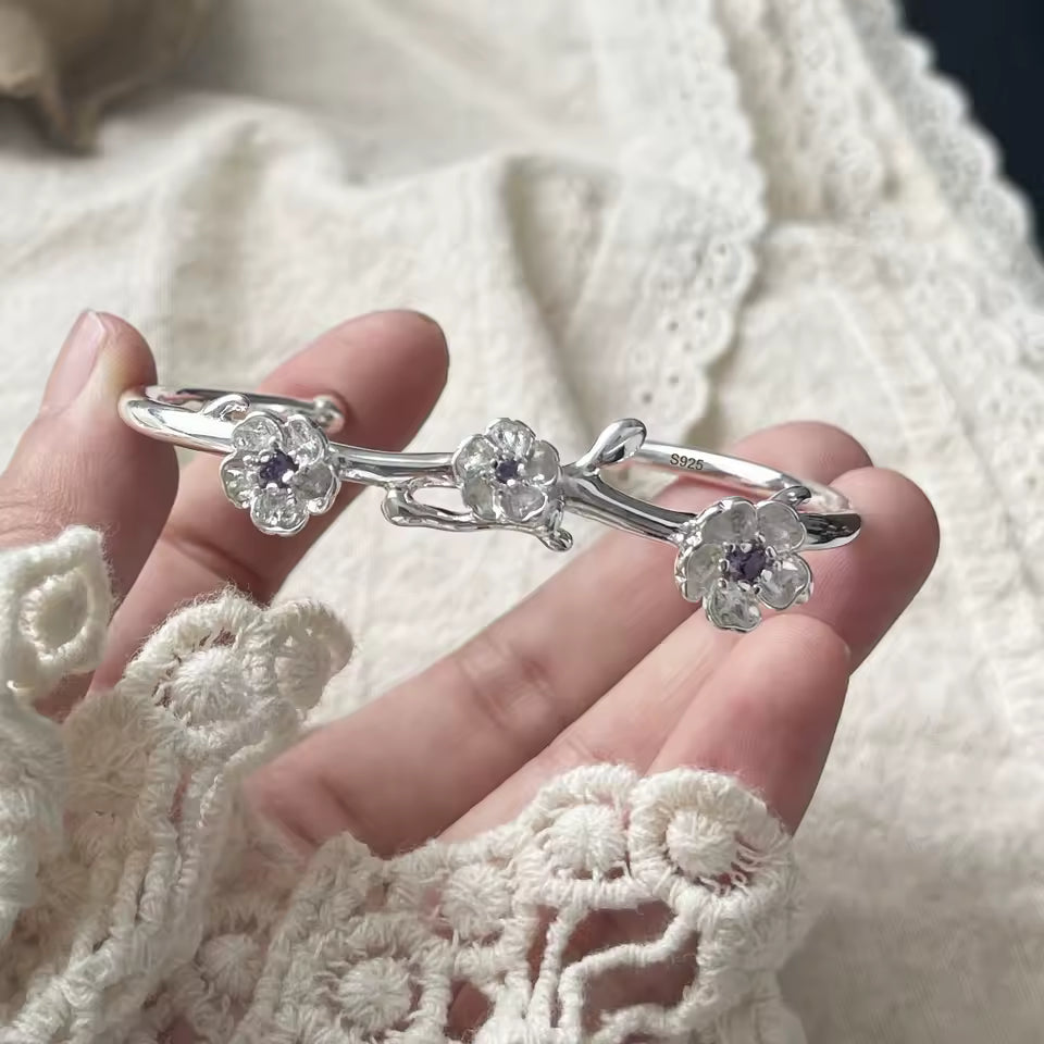 Silver bracelet with floral designs held by a hand against a white lace fabric background