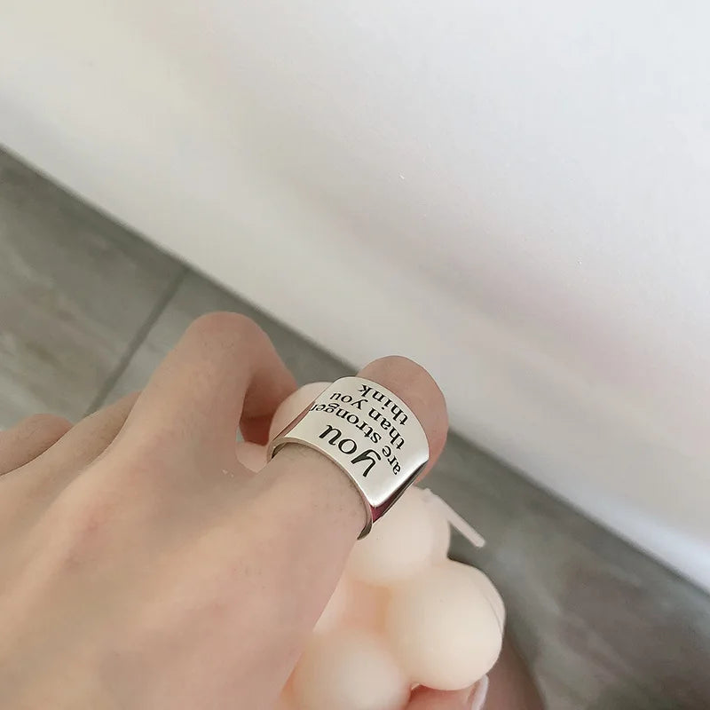 Hand wearing a silver ring with engraved text on a neutral background