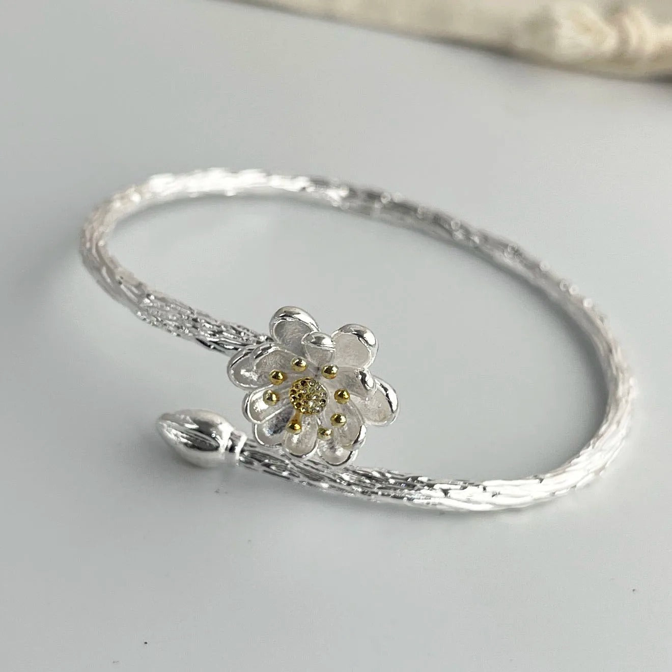 Silver bracelet with a floral charm on a light gray background