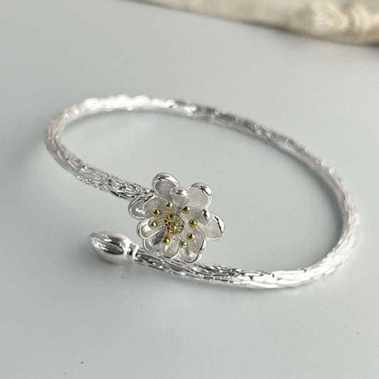 Silver bracelet with a floral charm on a light gray background