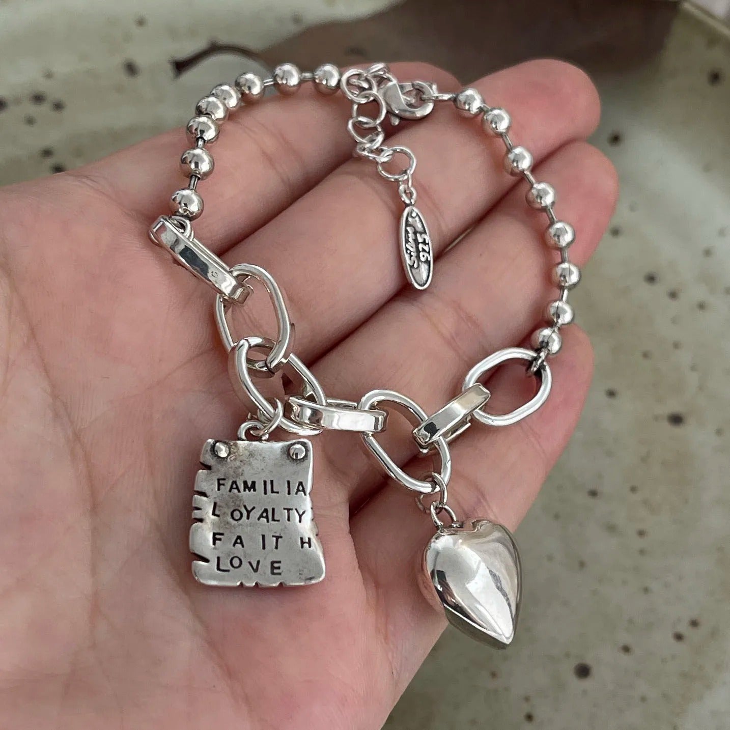 Silver bracelet with charms held in a hand against a neutral background