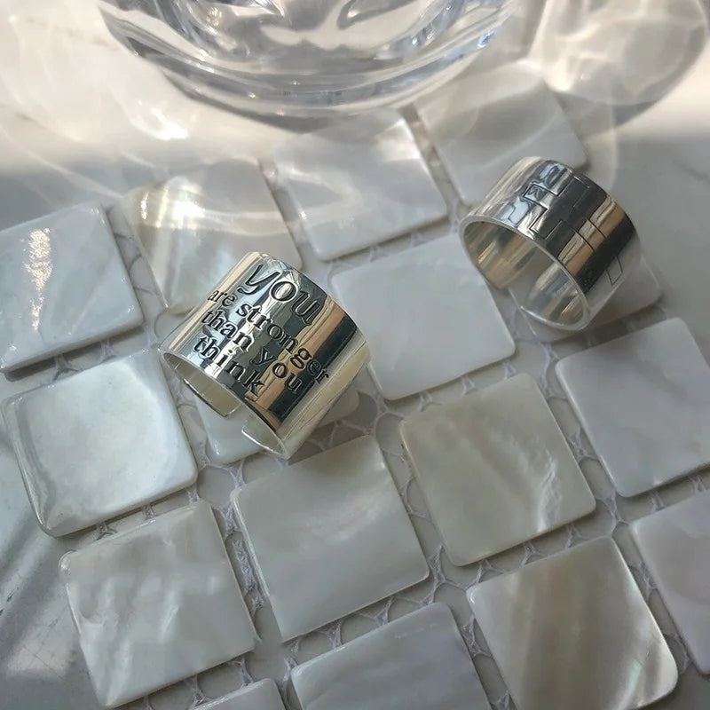 Silver rings with engraved text on a white mosaic tile surface