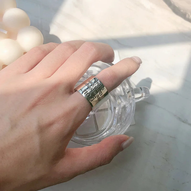 Hand wearing a silver ring with text on a light background