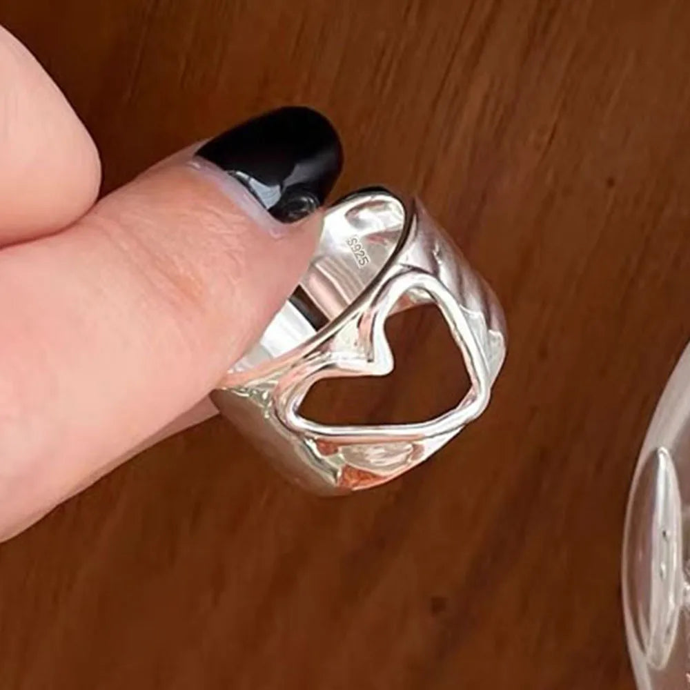 Silver hear ring held by a hand with black nail polish on a wooden surface