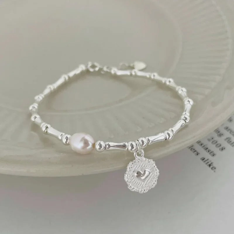 Silver bracelet with a pink pearl and a heart charm on a light background