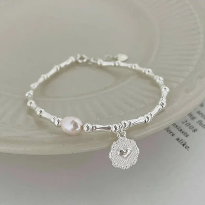 Silver bracelet with a pink pearl and a heart charm on a light background
