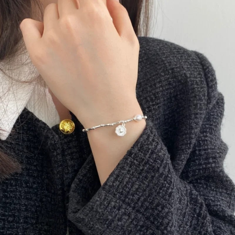 Hand wearing a silver bracelet with a white round charm, against a neutral background.