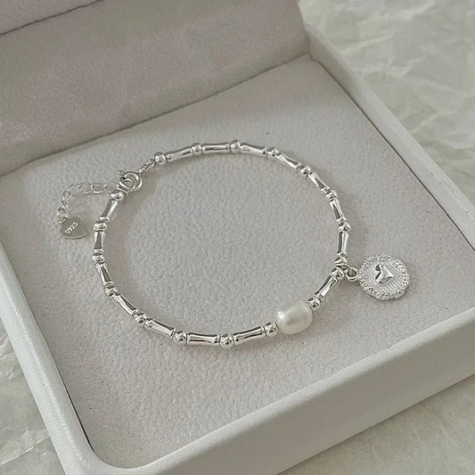 Silver bracelet with a pearl charm on a light gray surface