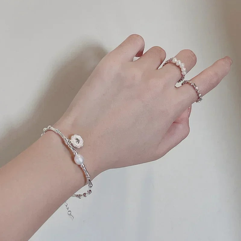 Hand wearing a pearl bracelet and ring on a plain background