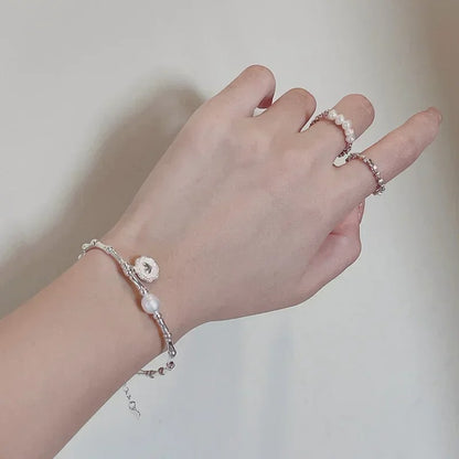 Hand wearing a pearl bracelet and ring on a plain background