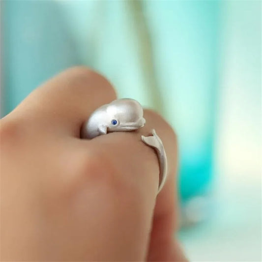 Silver dolphin-shaped ring on a person's finger with a blurred background