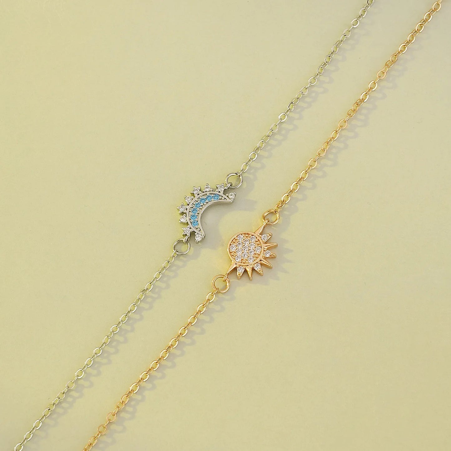 Two gold necklaces with sun and moon pendants on a light green background