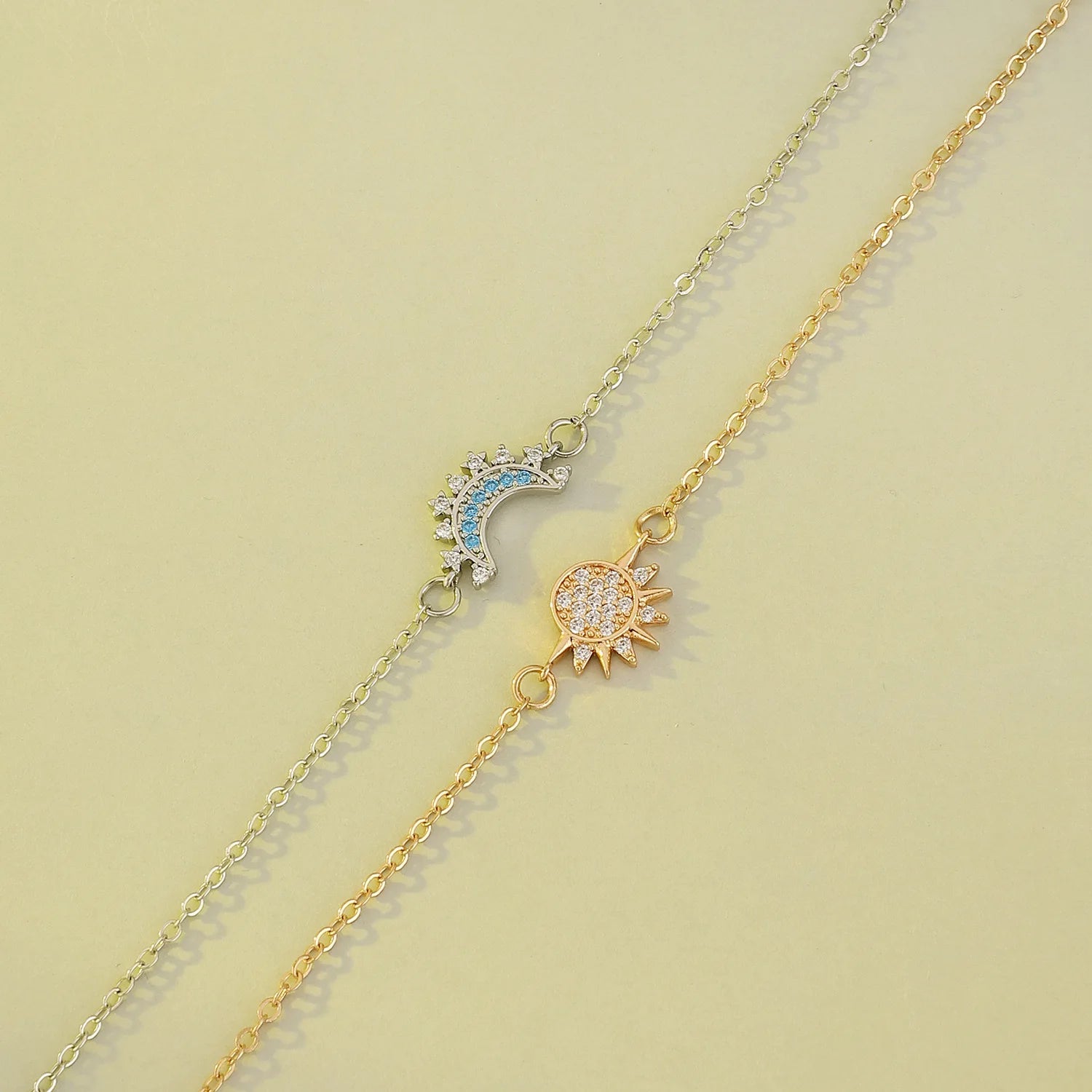 Two gold necklaces with sun and moon pendants on a light green background