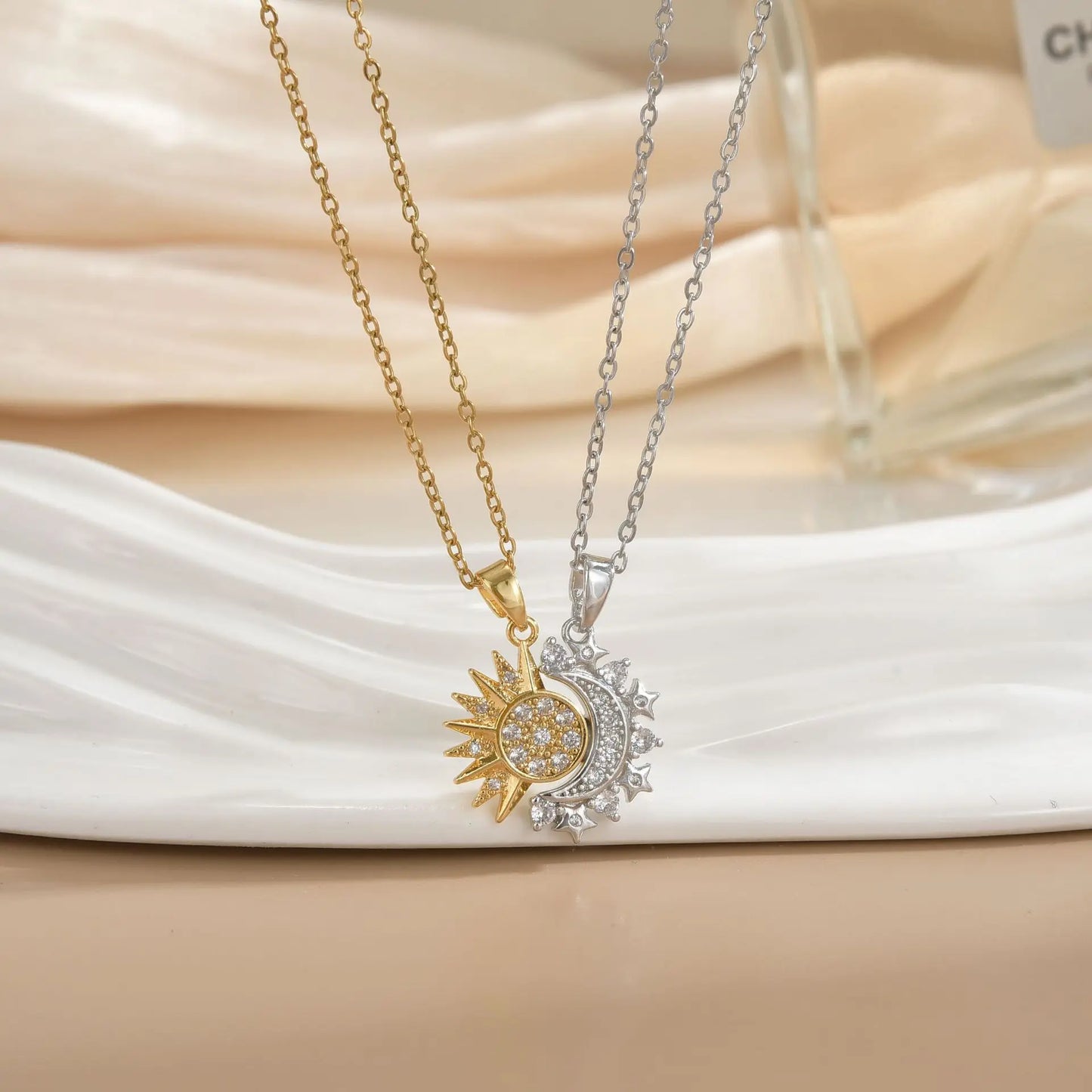 Two necklaces with sun and moon pendants on a white fabric background