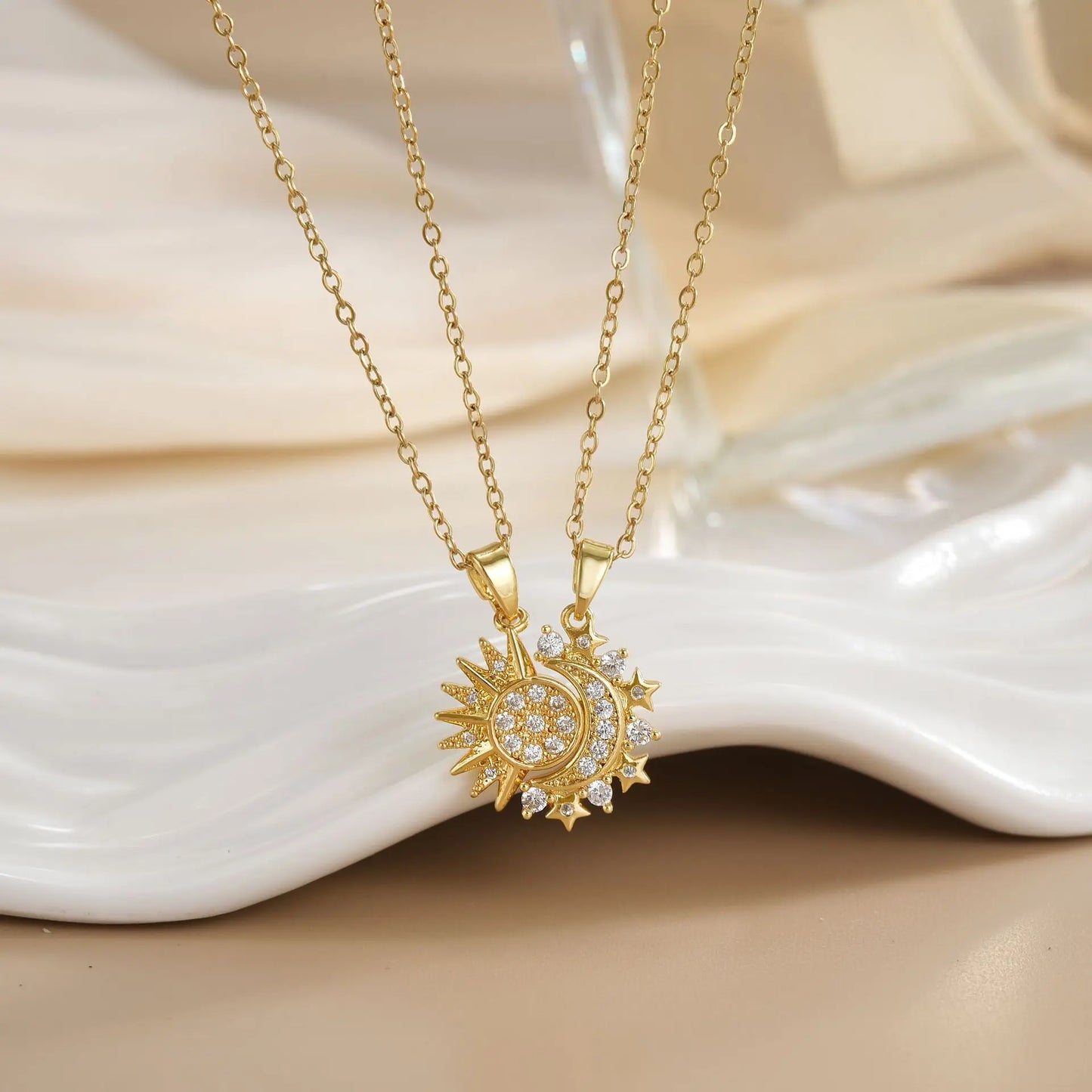 Gold necklaces with moon and sun pendants on a white shell background