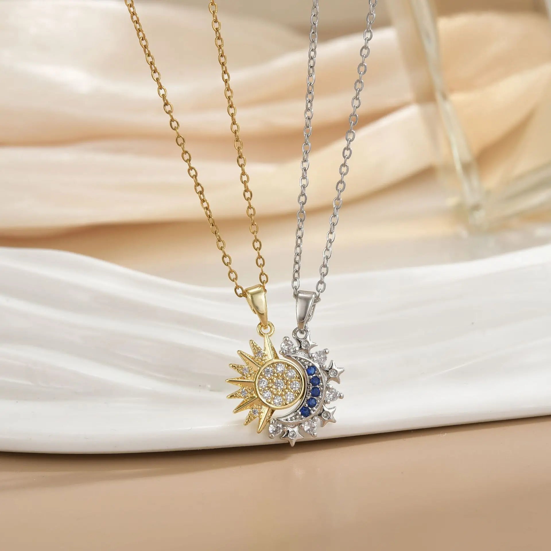 Two necklaces with sun and moon pendants on a white fabric background