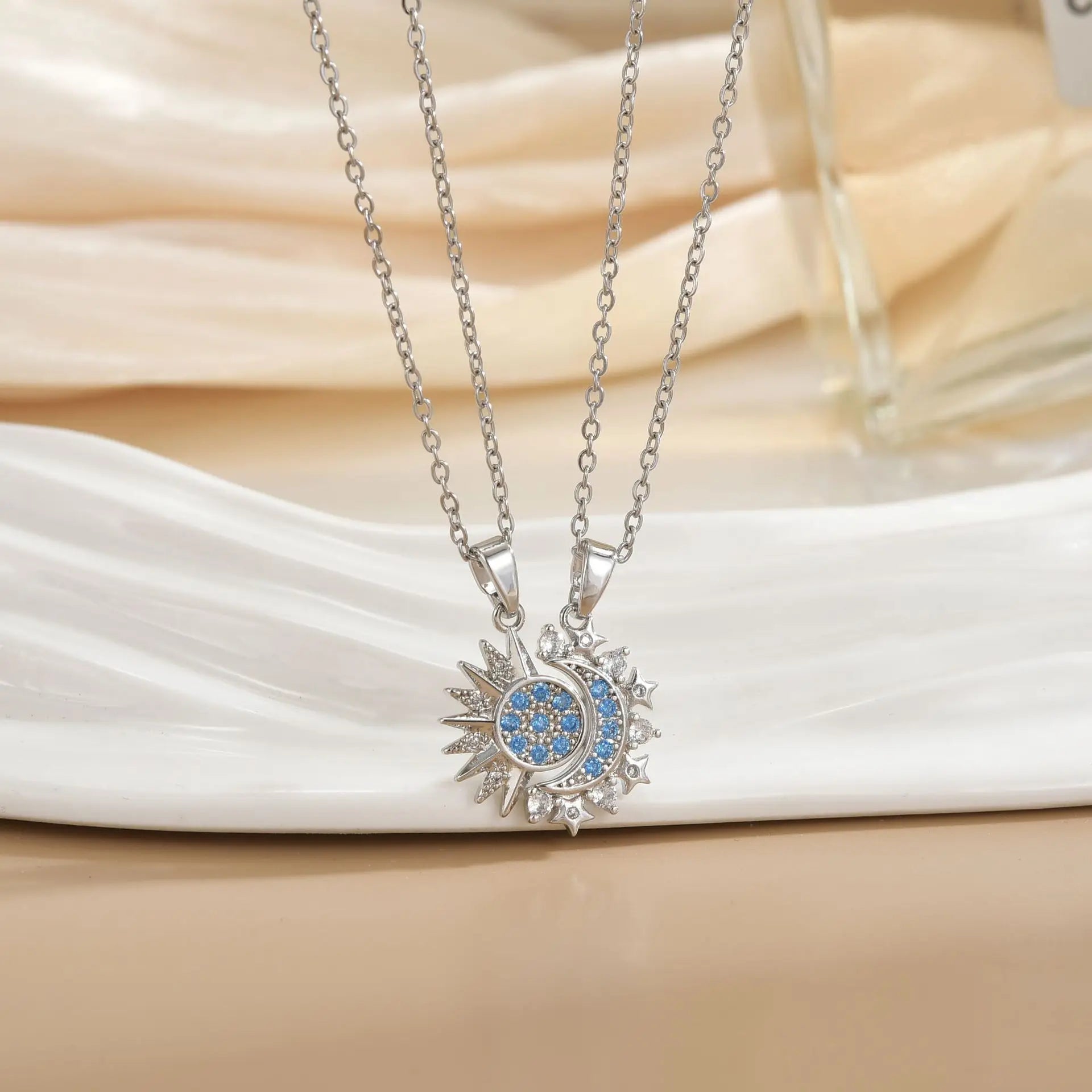 Silver necklace with a sun and moon pendant featuring blue stones on a white fabric background