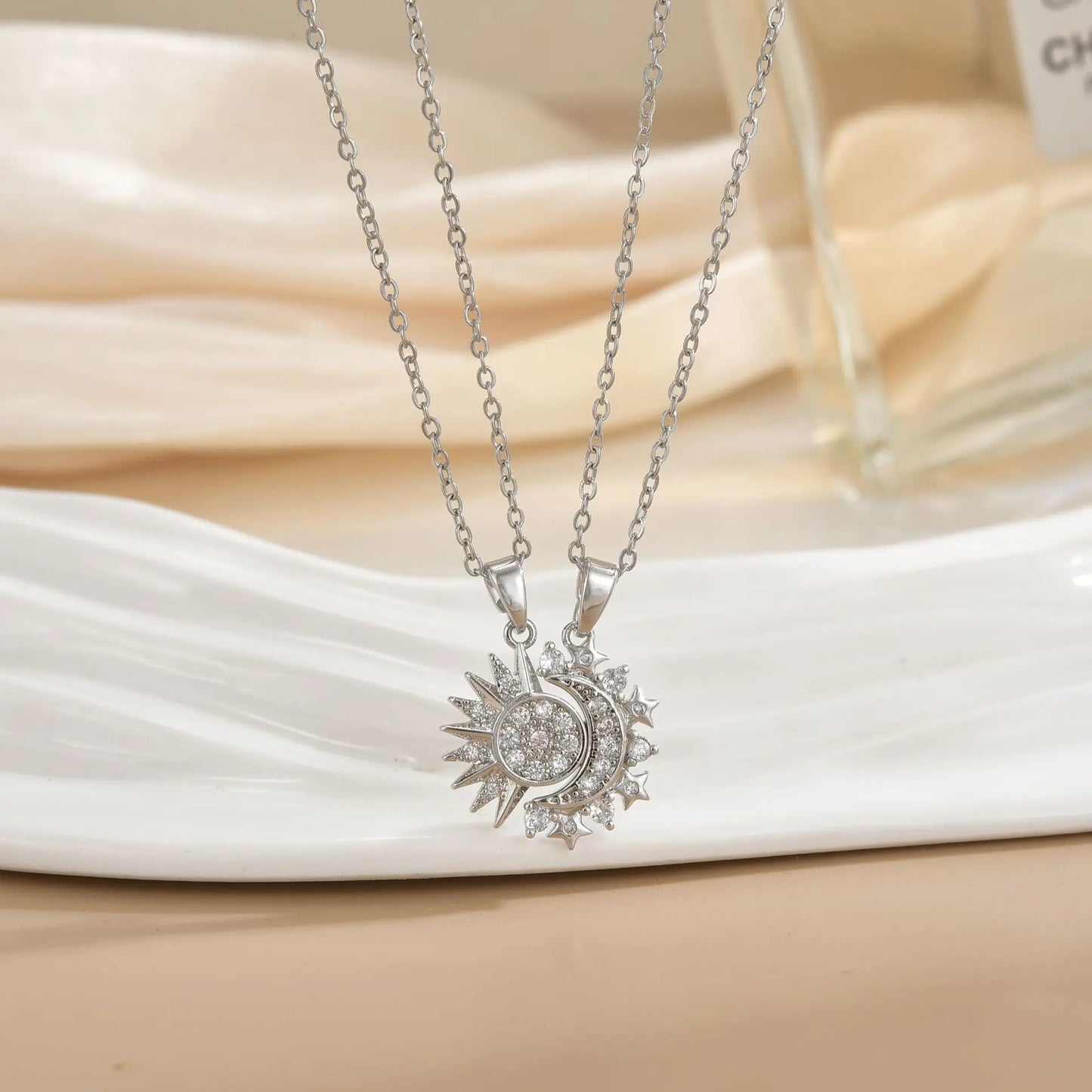 Silver necklace with sun and moon pendant on a white fabric background