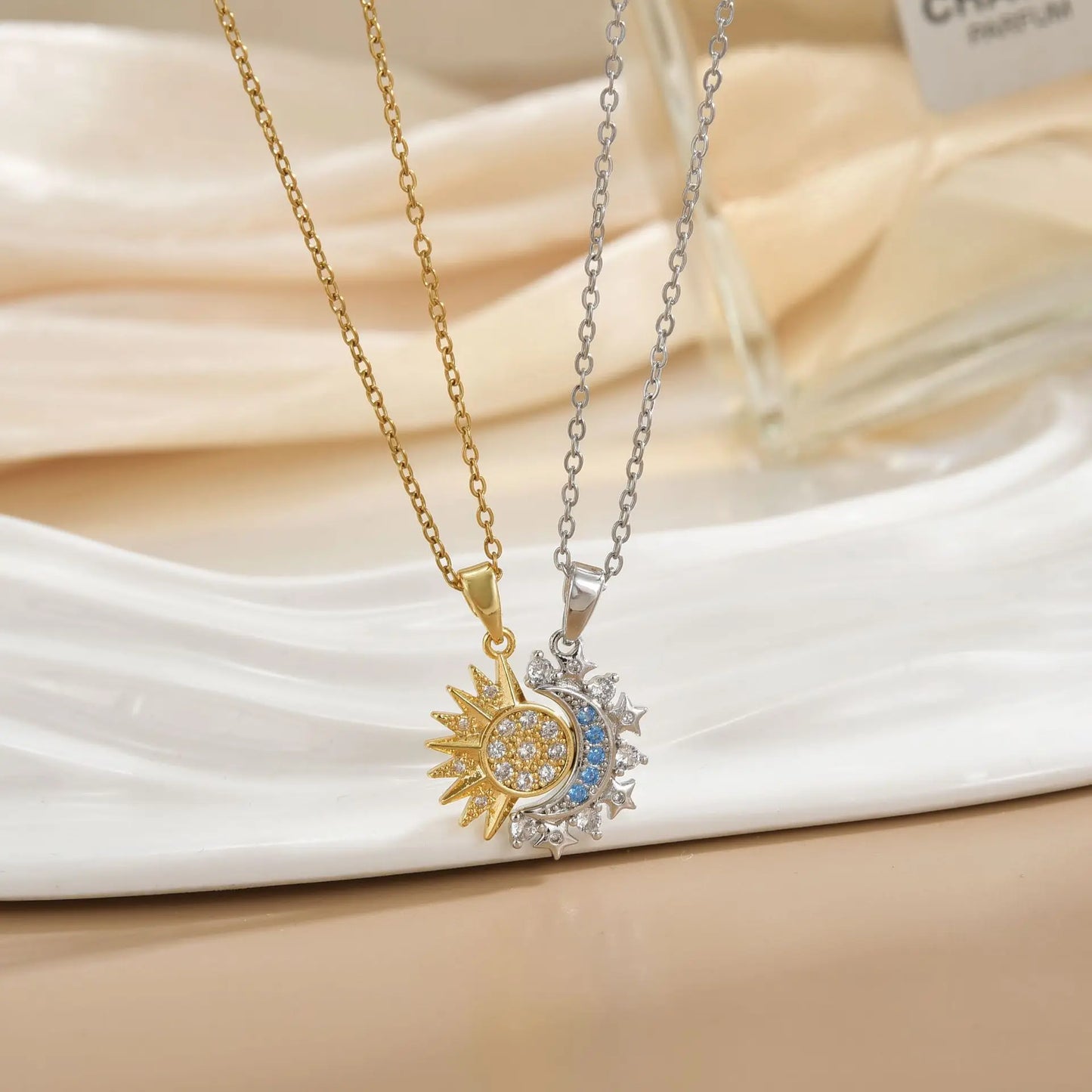 Two necklaces with sun and moon pendants on a beige fabric background