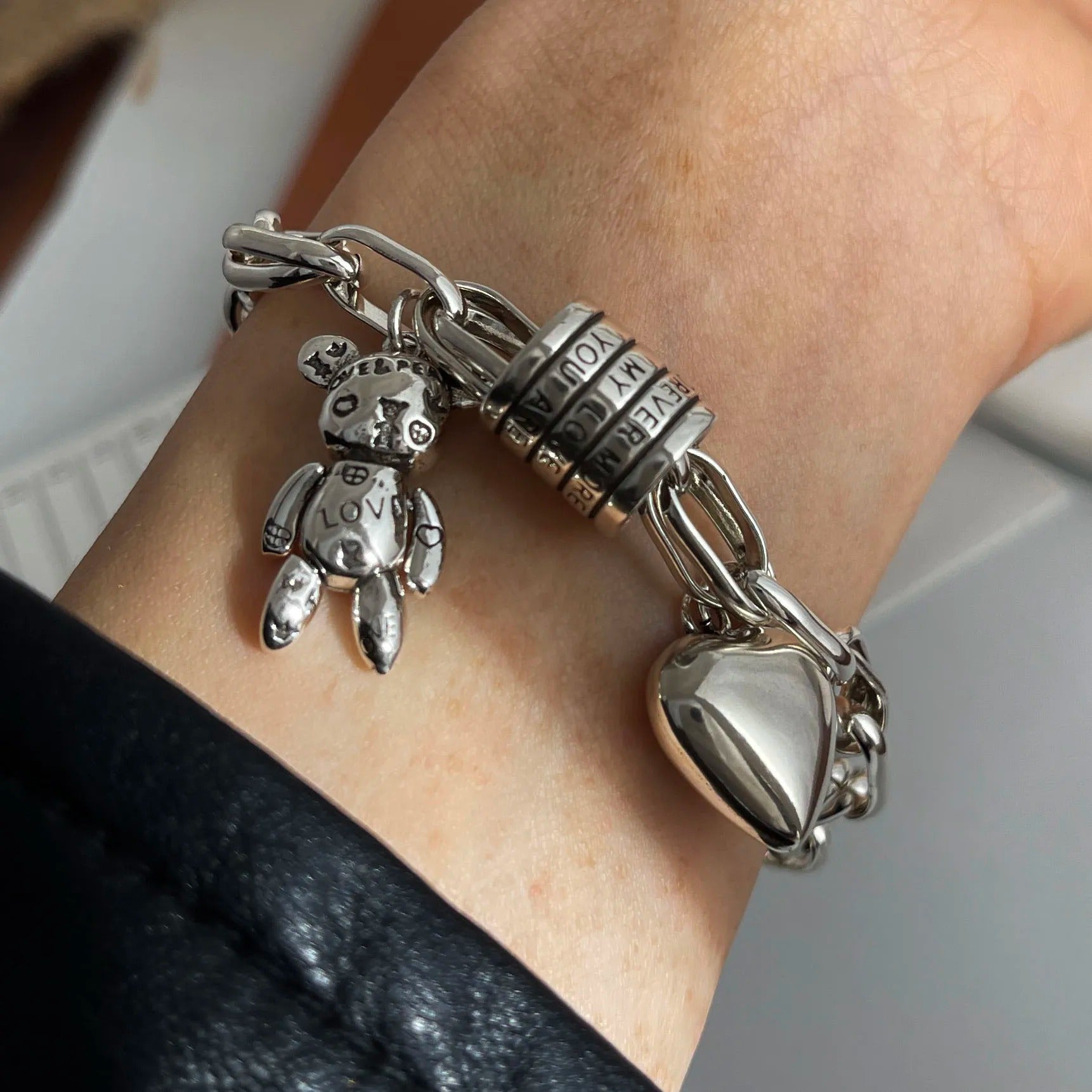 Silver bracelet with charms on a wrist against a neutral background