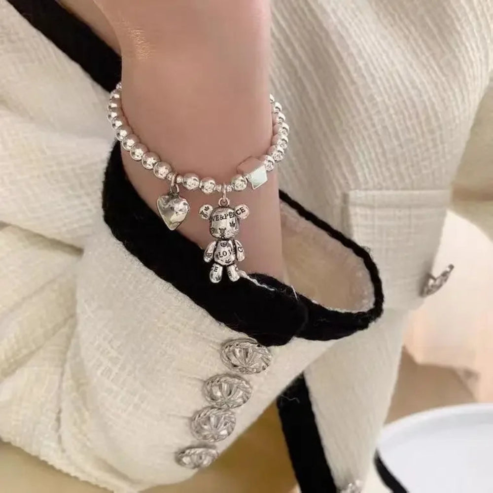 Close-up of a foot wearing a anklet with a teddy bear charm, against a neutral background.