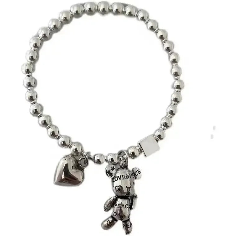 Silver beaded bracelet with heart and teddy bear charm on a white background