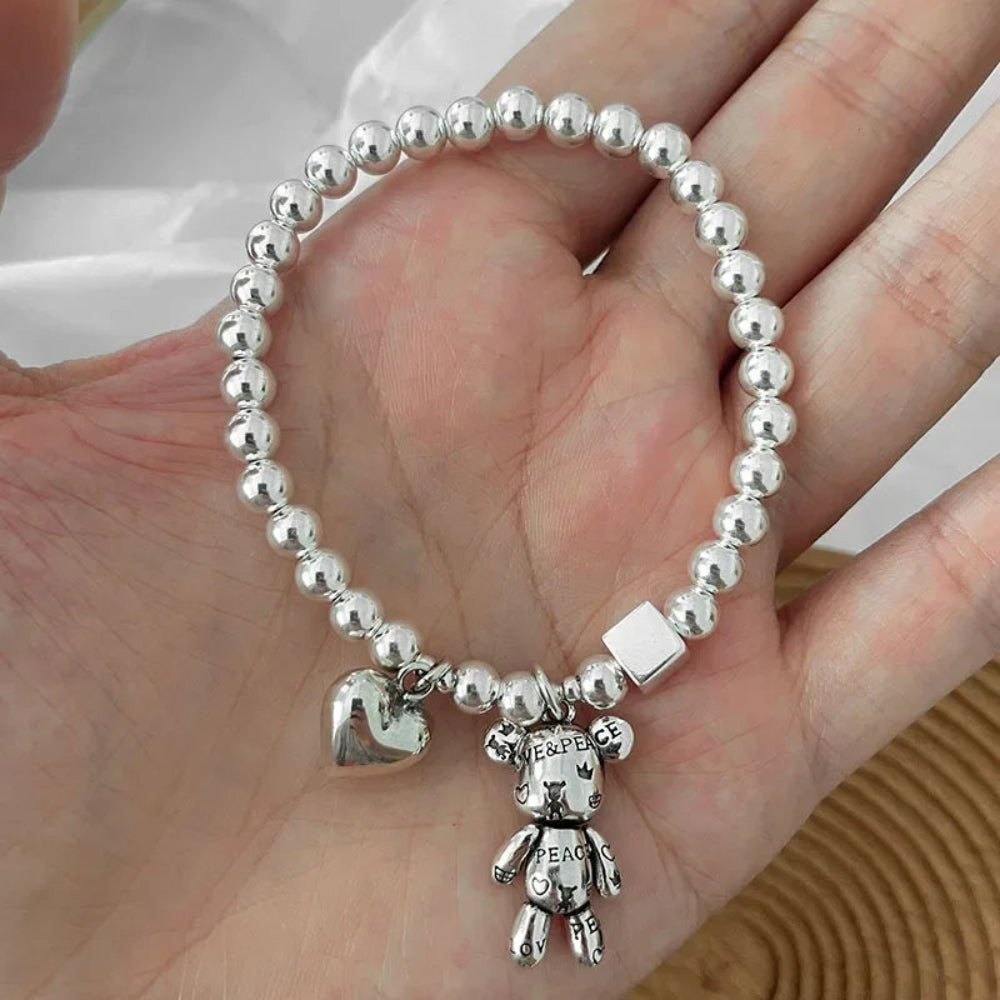 Silver beaded bracelet with a teddy bear charm held in a hand.